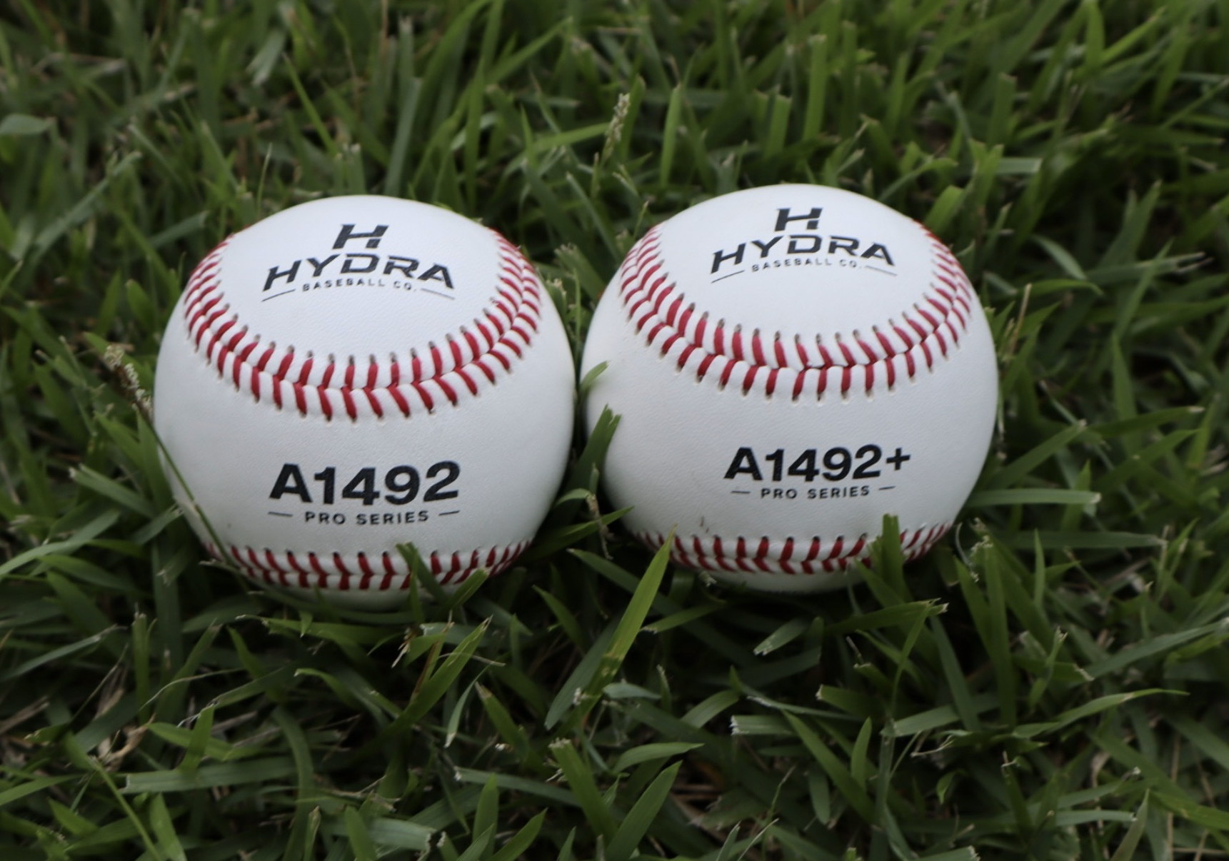 A Hydra A1492 practice ball and an A1492+ game ball side by side in the grass